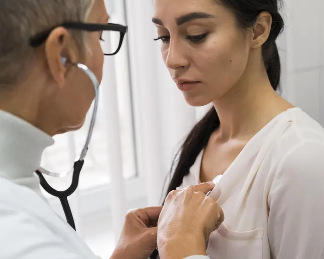 Médica escucha con estetoscopio a una paciente adulta durante un examen físico