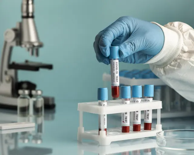 Técnico de laboratorio con guantes sostiene un tubo de muestra junto a un microscopio